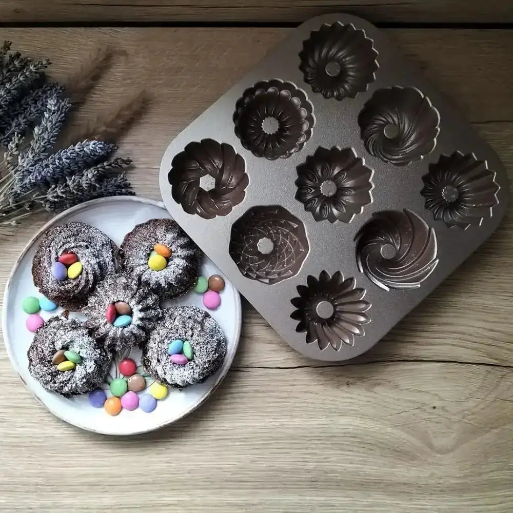 Metal cake mold with decorative patterns next to a plate of small round cakes on a wooden surface.