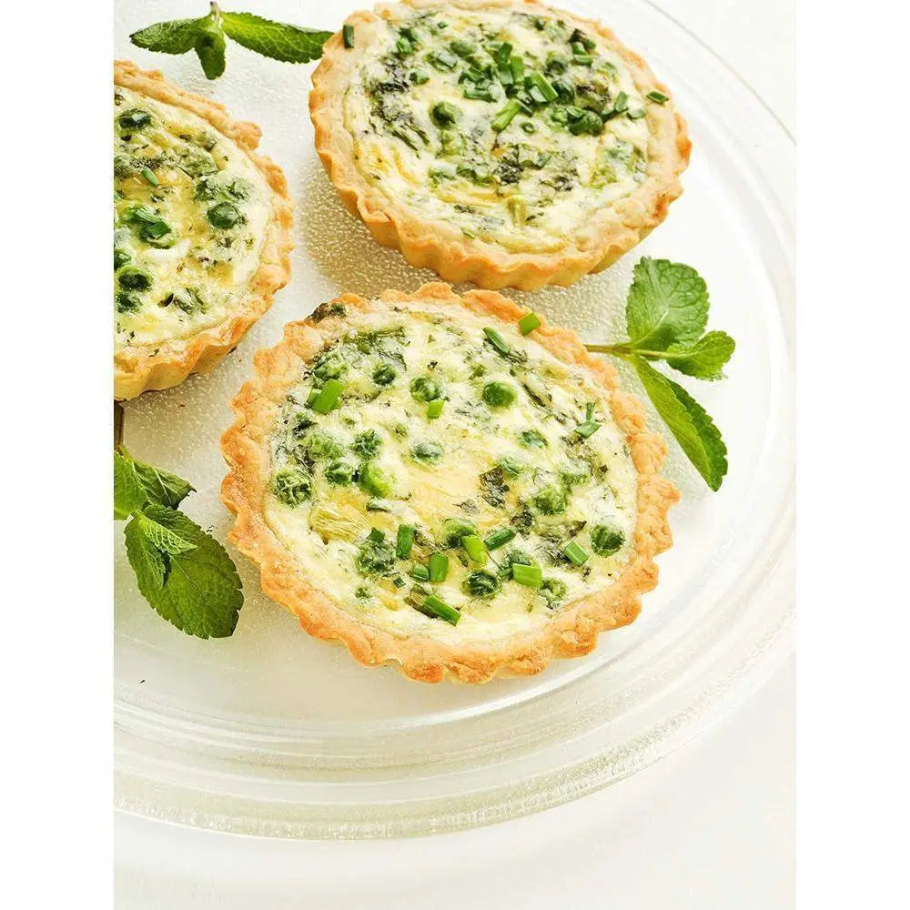 Three small green vegetable tarts on a white plate with fresh herbs.