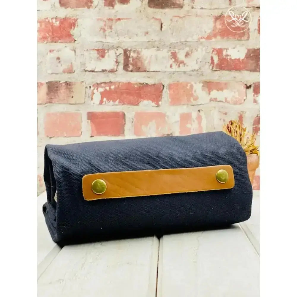 Navy blue roll-up bag with a brown leather strap against a brick wall background