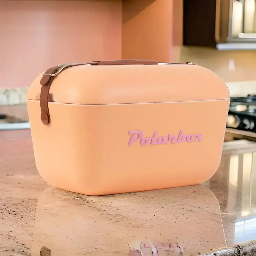 A peach-colored polarbox classic retro cooler box 20l with brown leather strap and pink embossed branding