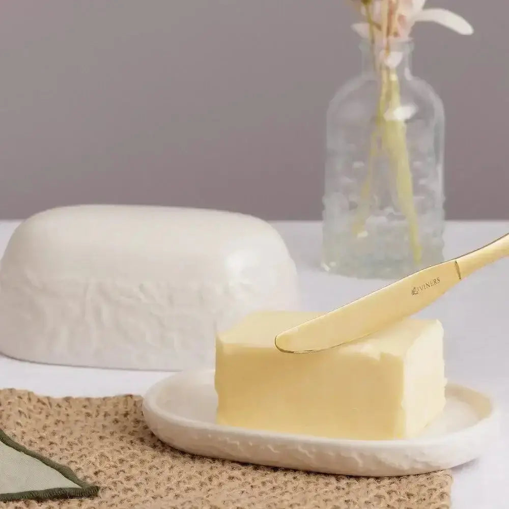 Gold-finished butter knife with engraved brand name resting on pale yellow butter from price and kensington acorn butter dish