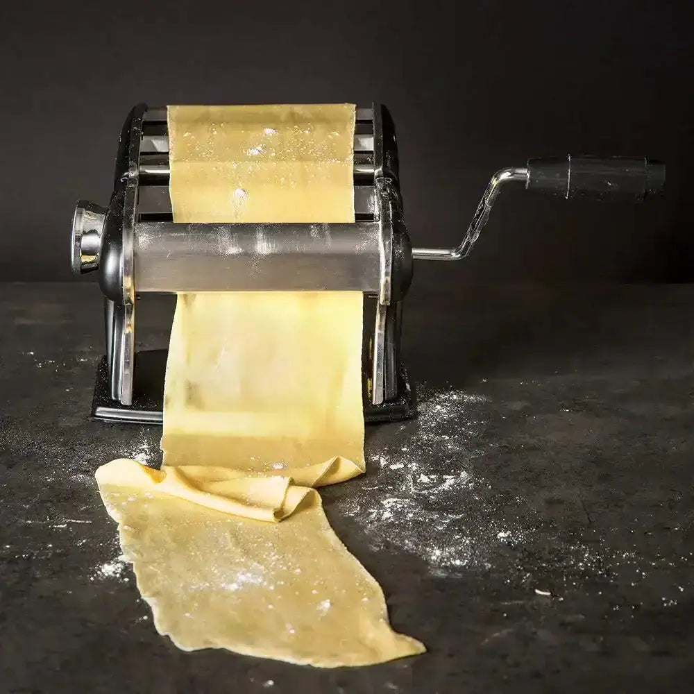 Pasta maker rolling out pasta sheets on a dark surface