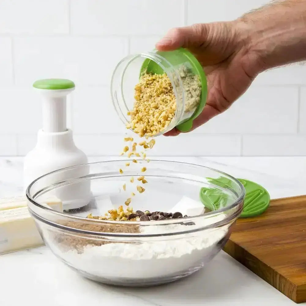 Hand pouring crushed garlic from a green container into a glass bowl on a kitchen counter.