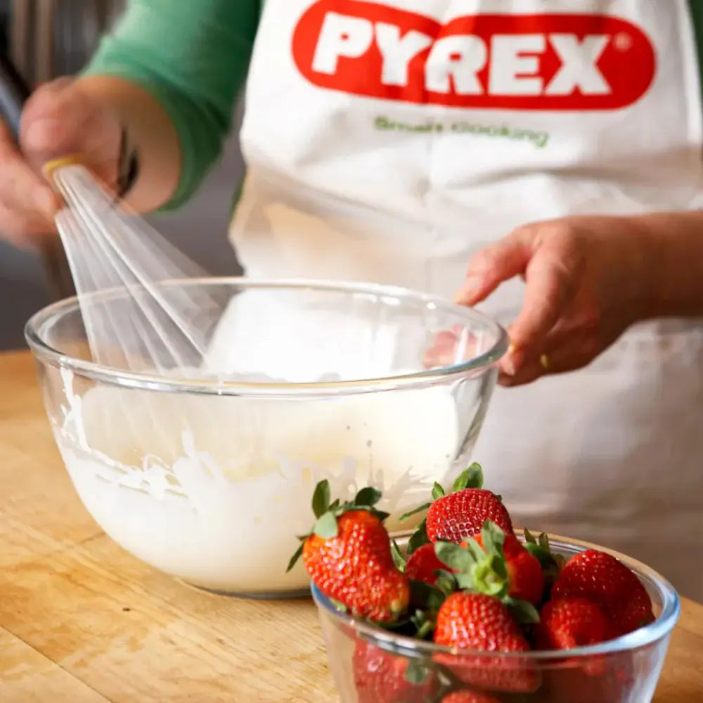 Person whisking batter in a Pyrex bowl with strawberries on a wooden surface