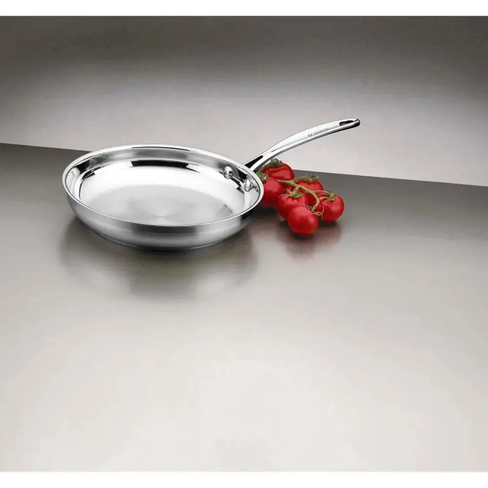 Stainless steel frying pan on a reflective surface with red grapes