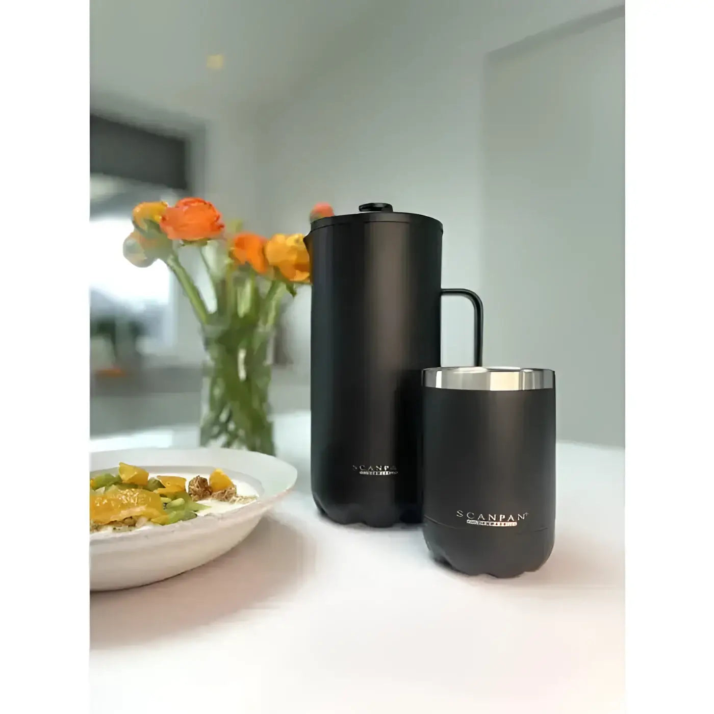 Black Scanvas insulated containers on a table with a dish and flowers in the background
