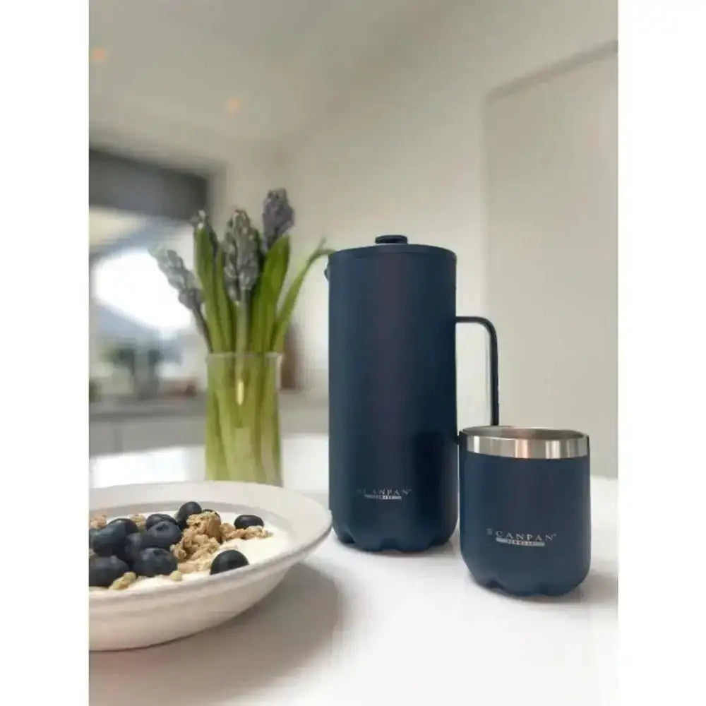 Two navy blue Scandinavia mugs on a kitchen counter with a bowl of cereal and flowers in the background.
