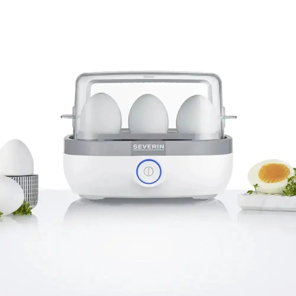 Electric egg boiler with clear lid holding six eggs, hard-boiled egg and herbs nearby