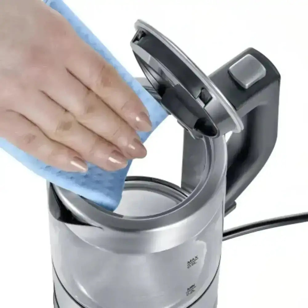 Person cleaning a silver electric kettle with a blue cloth.