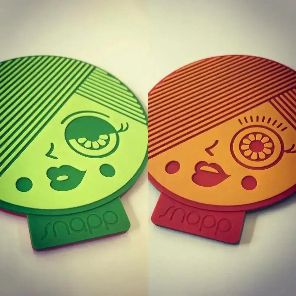 Two colorful coasters with face designs and 'snapp' branding on a light background