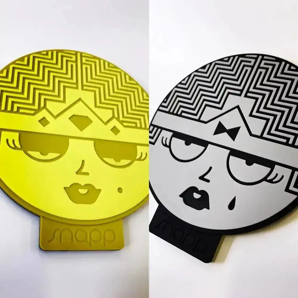 Yellow and black stylized face-shaped silicone phone stand with geometric hair and snapp brand base from snap design coaster set