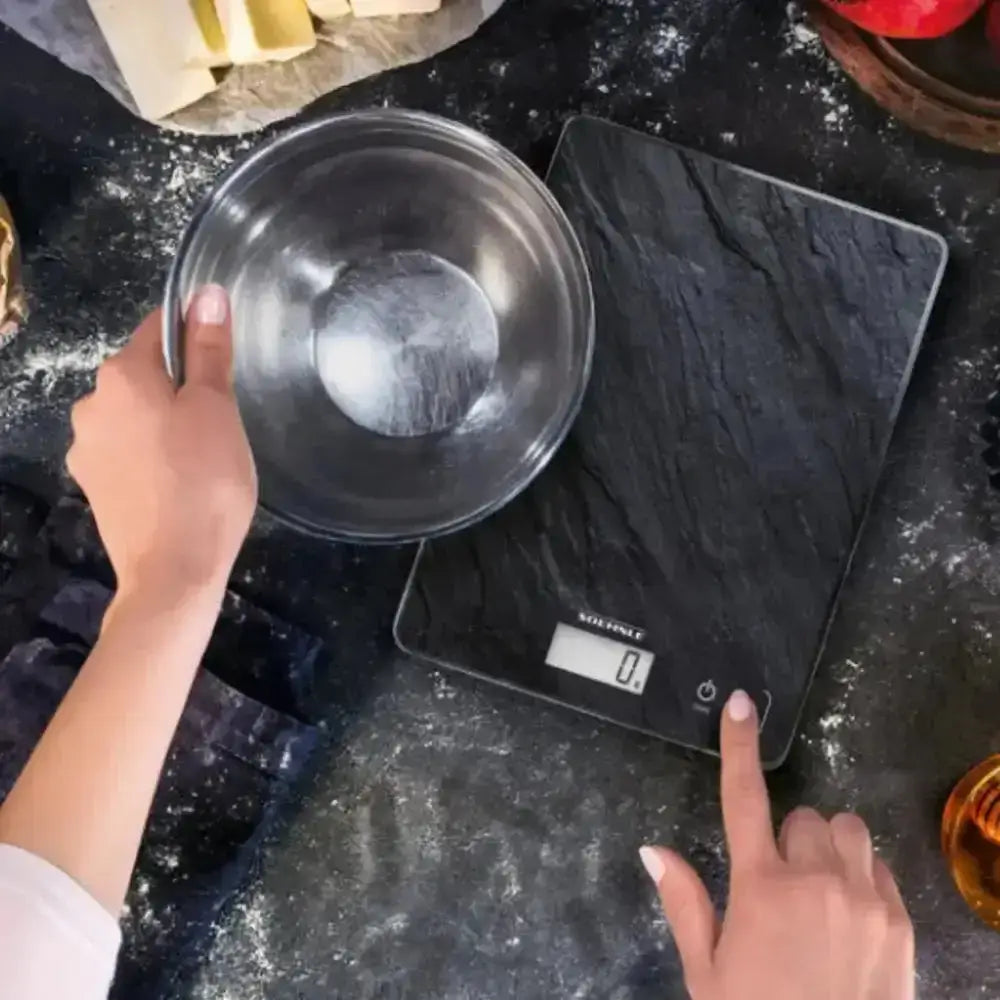Digital kitchen scale with slate surface, bowl on top, hands using controls, baking setting