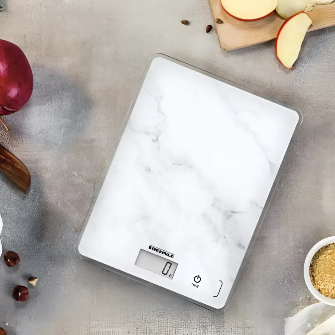 Digital kitchen scale with marble design on countertop, surrounded by apples and baking ingredients
