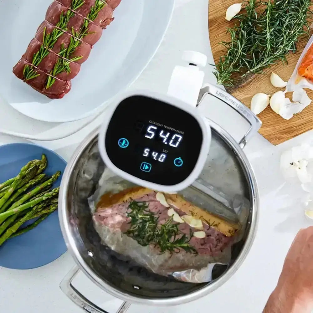 Digital thermometer inserted into a piece of meat with cooking ingredients around on a white surface.