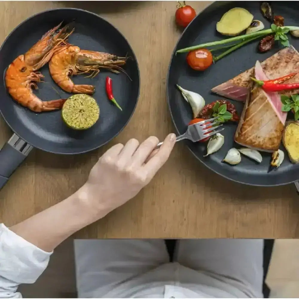 A hand holding a silver fork over grilled salmon in a squality biotan 24cm silver non-stick frying pan