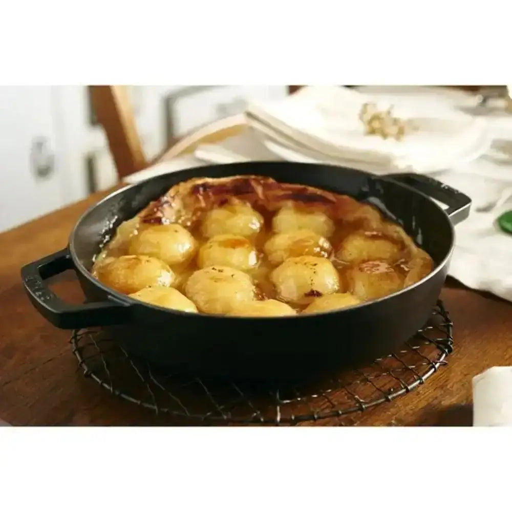 Staub cast iron braising pan 26cm black with two handles containing golden baked dumplings in glossy sauce