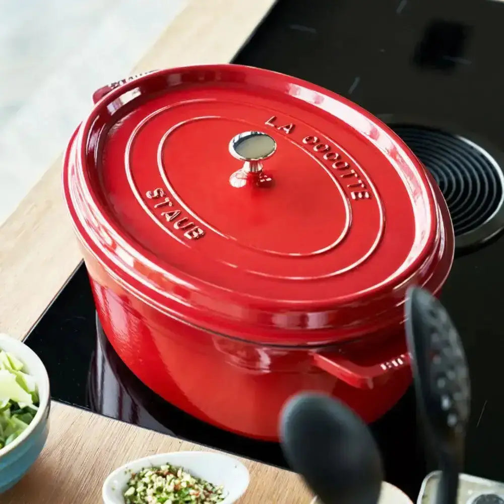 Red Staub cookware on a stove with ingredients and utensils around