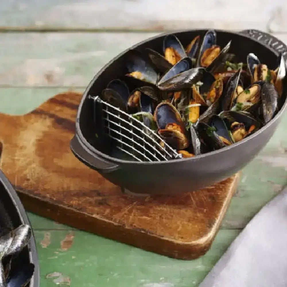 Black Staub oval cast iron mussel pot 2L with wire mesh strainer filled with cooked mussels in a skillet style