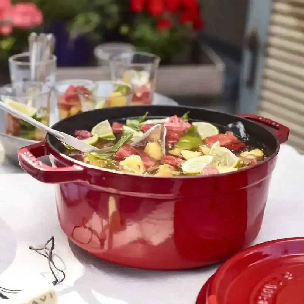 Staub round cast iron casserole pot 3.8l red with black interior filled with colorful meat and citrus stew