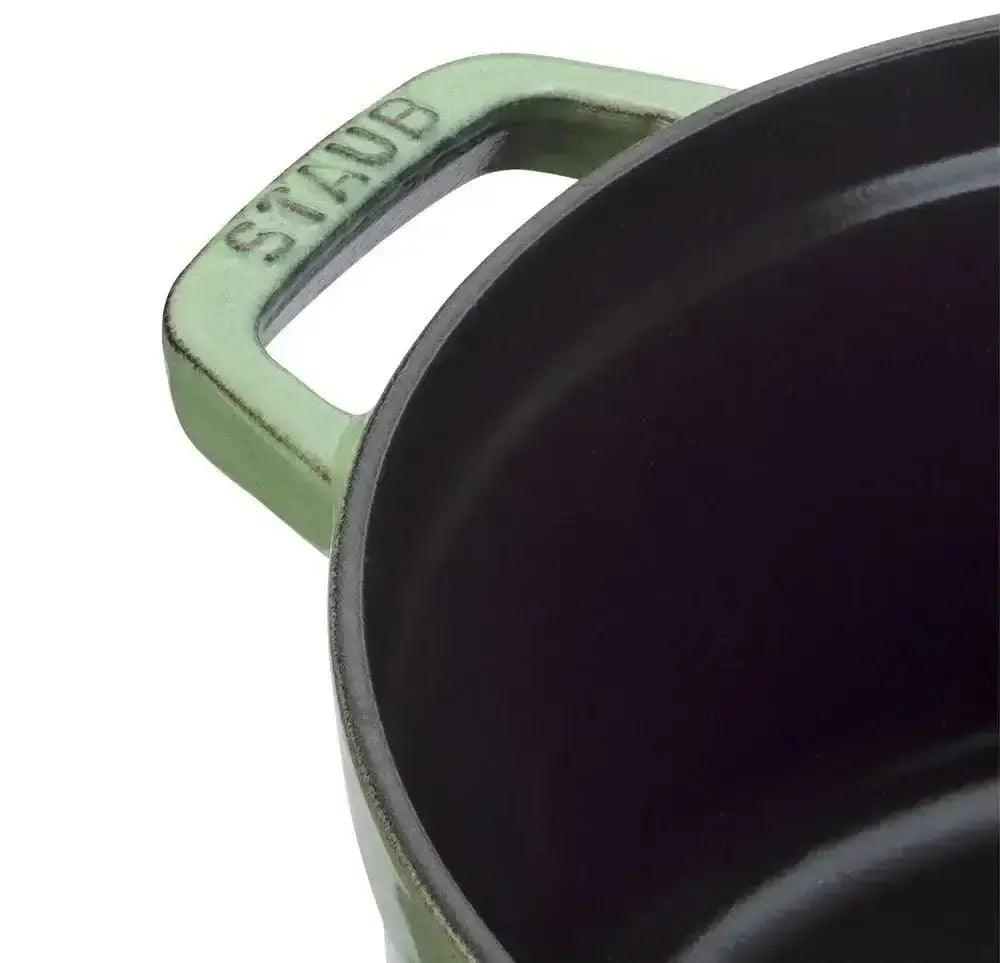 A matte sage green staub round cast iron casserole pot with a sturdy rectangular handle and 6.7 liter capacity