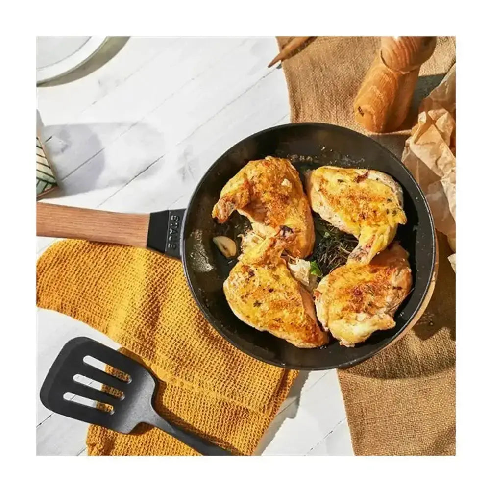 Black non-stick Staub cast iron frying pan 28cm with wooden handle and bonjour brand holding roasted chicken pieces