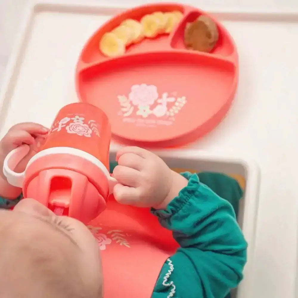Child holding a red cup with a matching tray containing food on a white surface