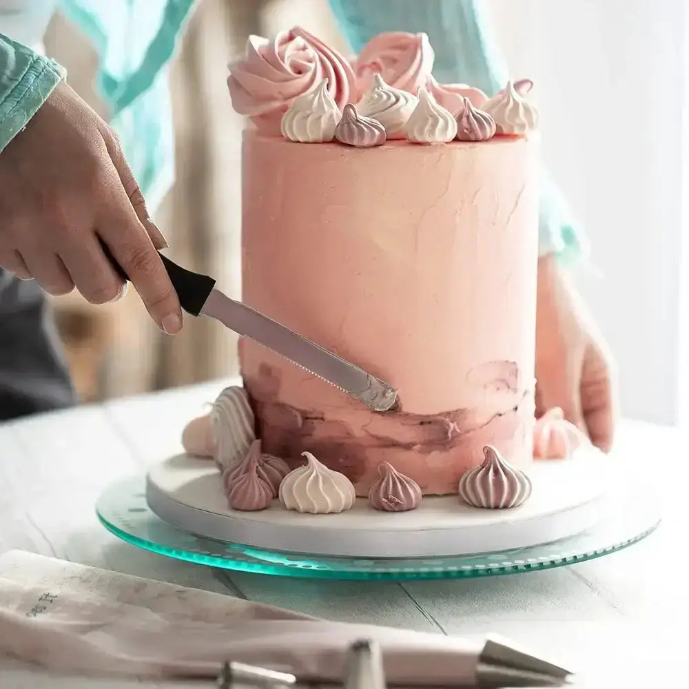 Person cutting a pink cake with white and pink decorations on a white plate.