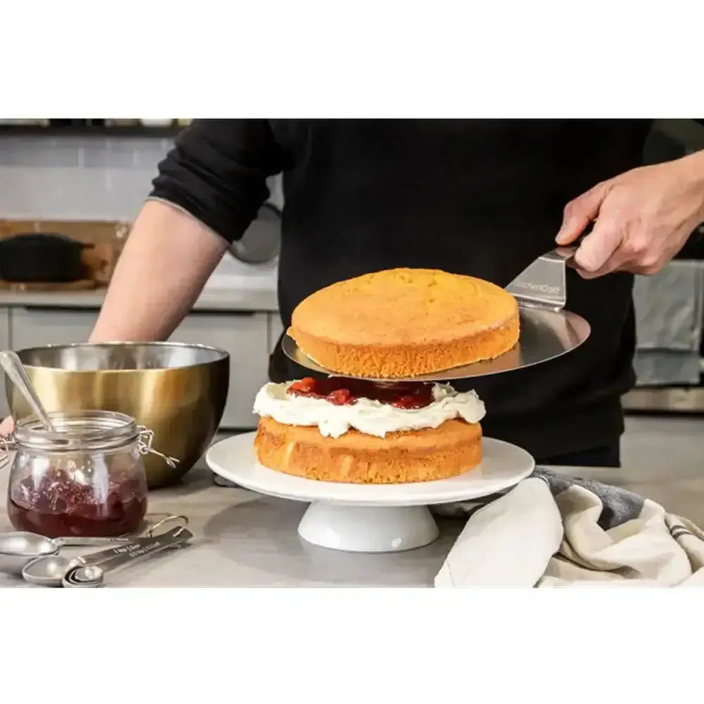Person cutting a layered cake with a spatula in a kitchen setting