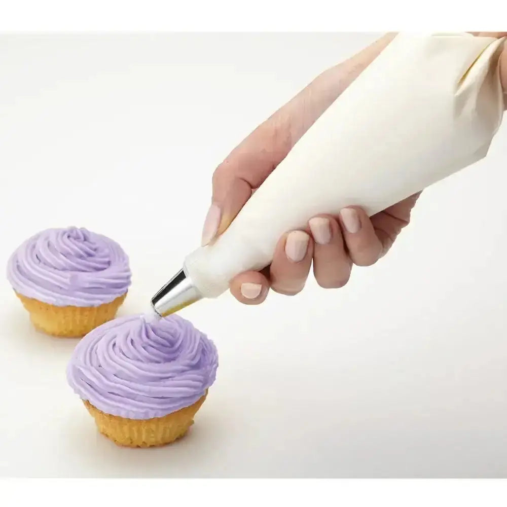 Hand using a piping bag to frost cupcakes with purple frosting on a white background