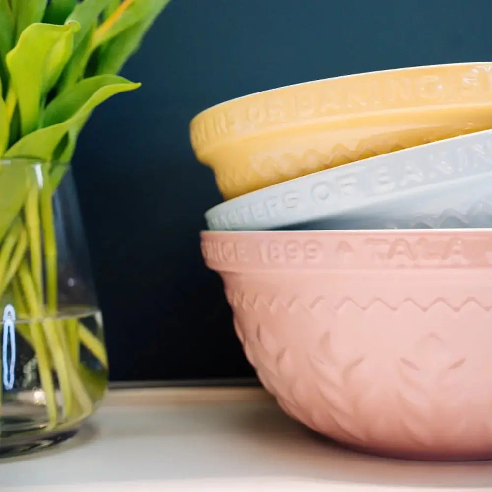 Stack of colorful bowls with a vase of green leaves on a dark background