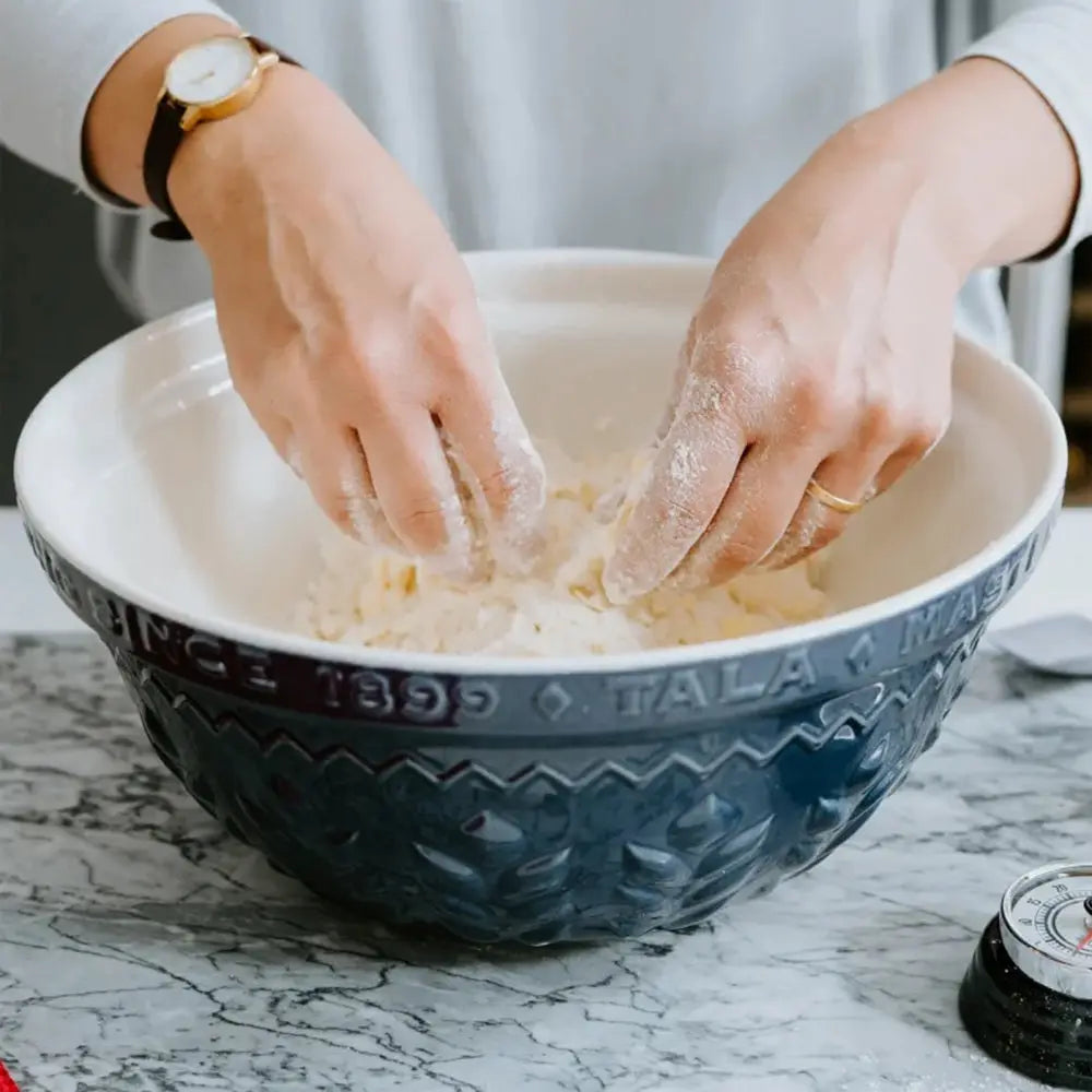 Person kneading dough in a blue Tala bowl on a marble countertop