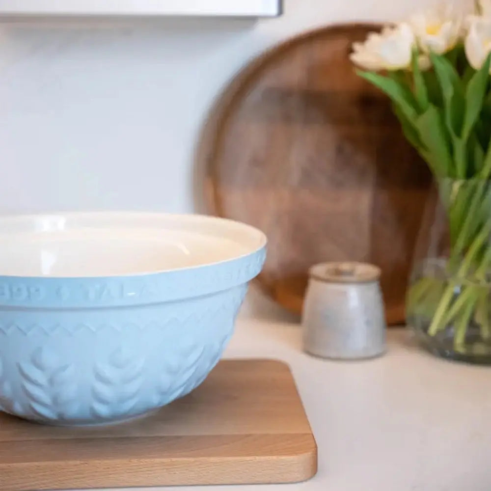 Blue bowl on a wooden cutting board with a vase of flowers in the background