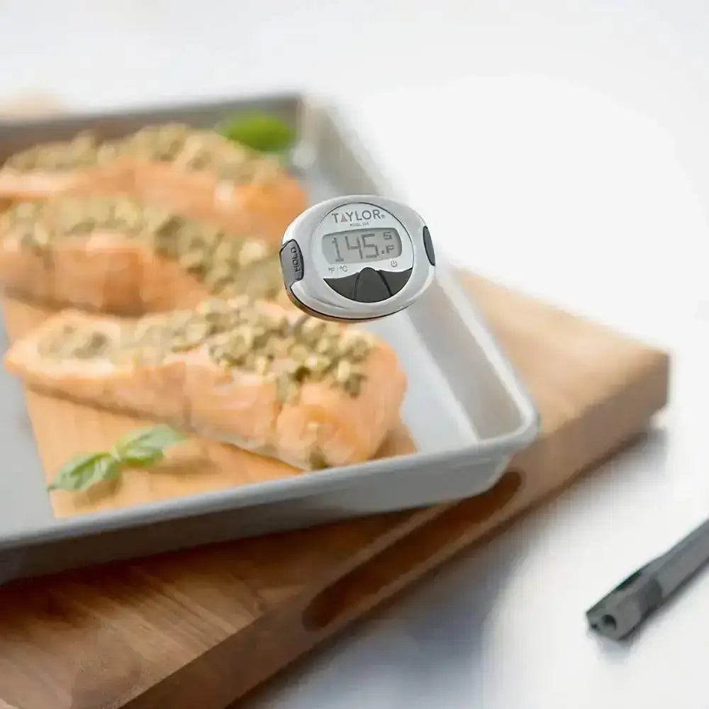 Digital kitchen thermometer with probe measuring cooked salmon on baking tray