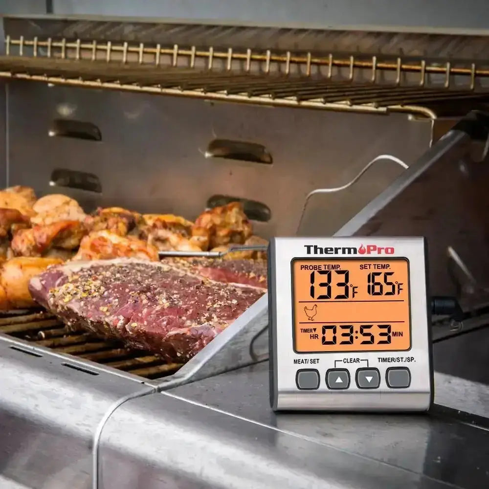 Thermometer on a grill displaying temperature and time, with food in the background.