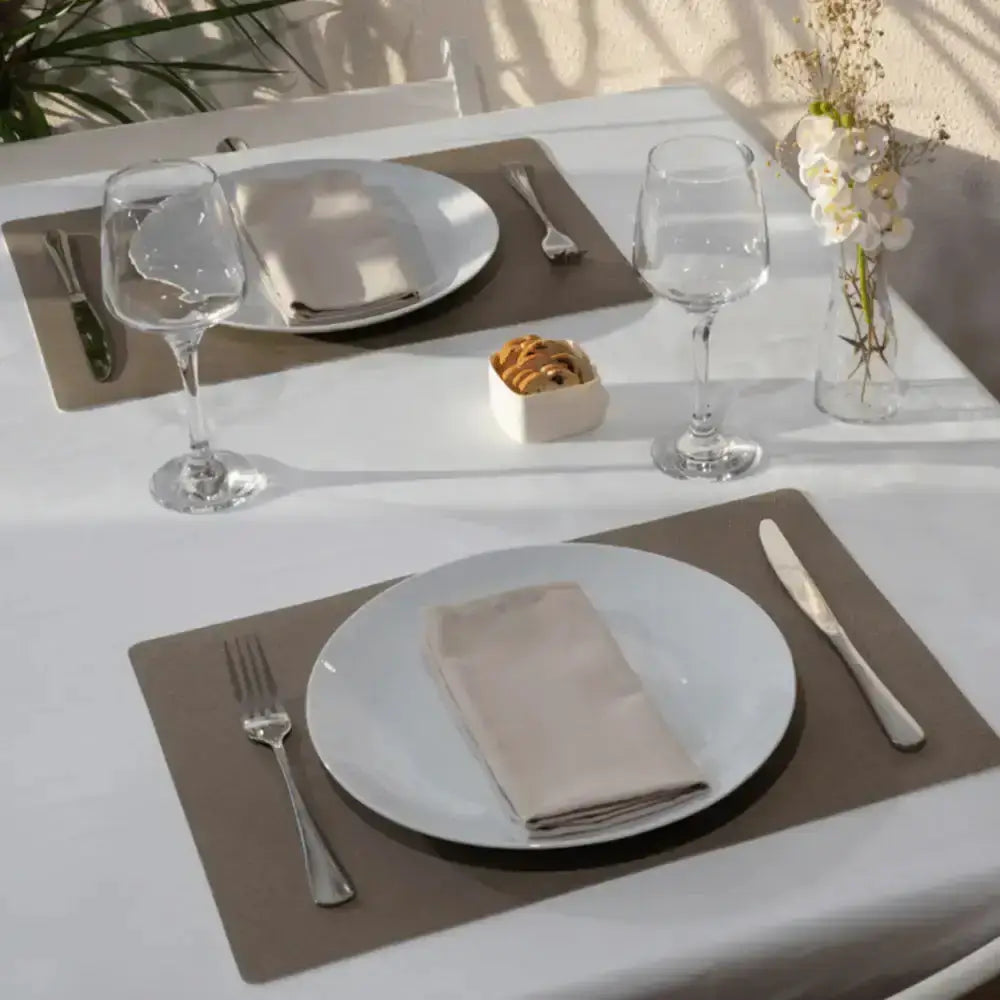 Dining table setting with plates, glasses, and cutlery on a white tablecloth.