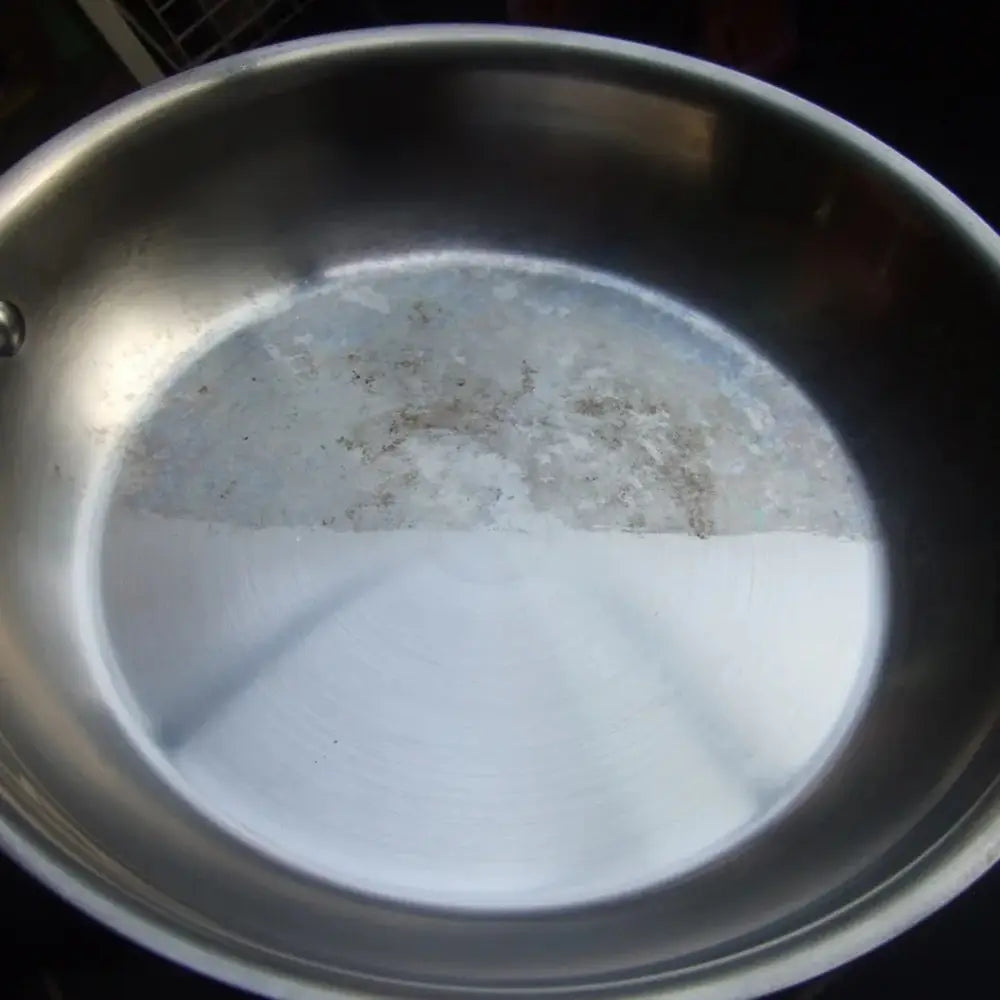 Stainless steel pan with one side cleaned, on a dark background