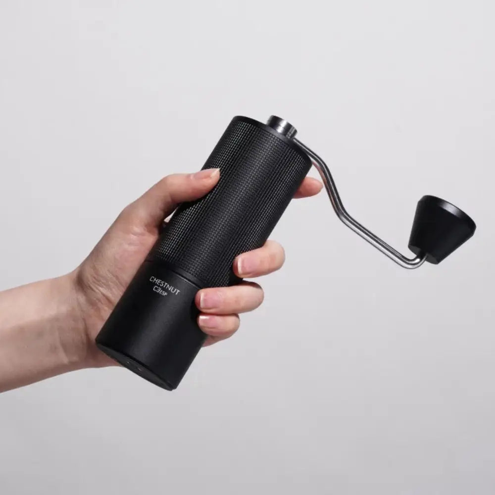 Hand holding a black manual coffee grinder against a light gray background