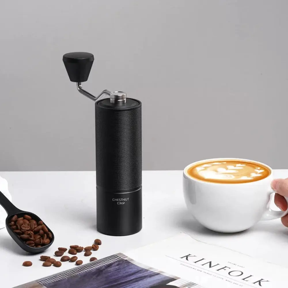 Black coffee grinder with coffee beans and a cup of coffee on a white surface.