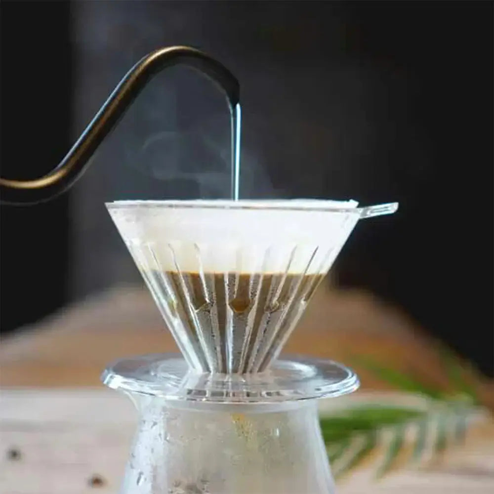 Coffee brewing process with a glass carafe and paper filter on a wooden surface.