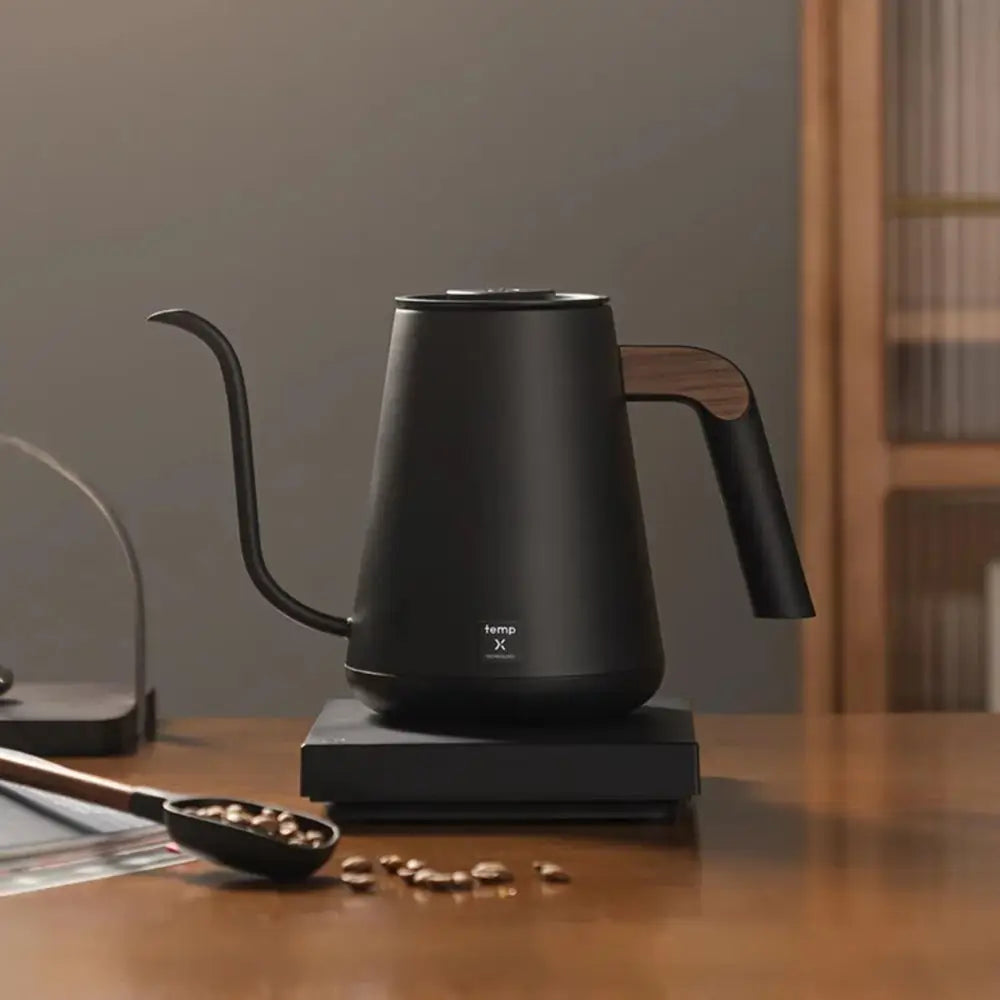 Black electric kettle on a wooden table with coffee beans and a spoon.