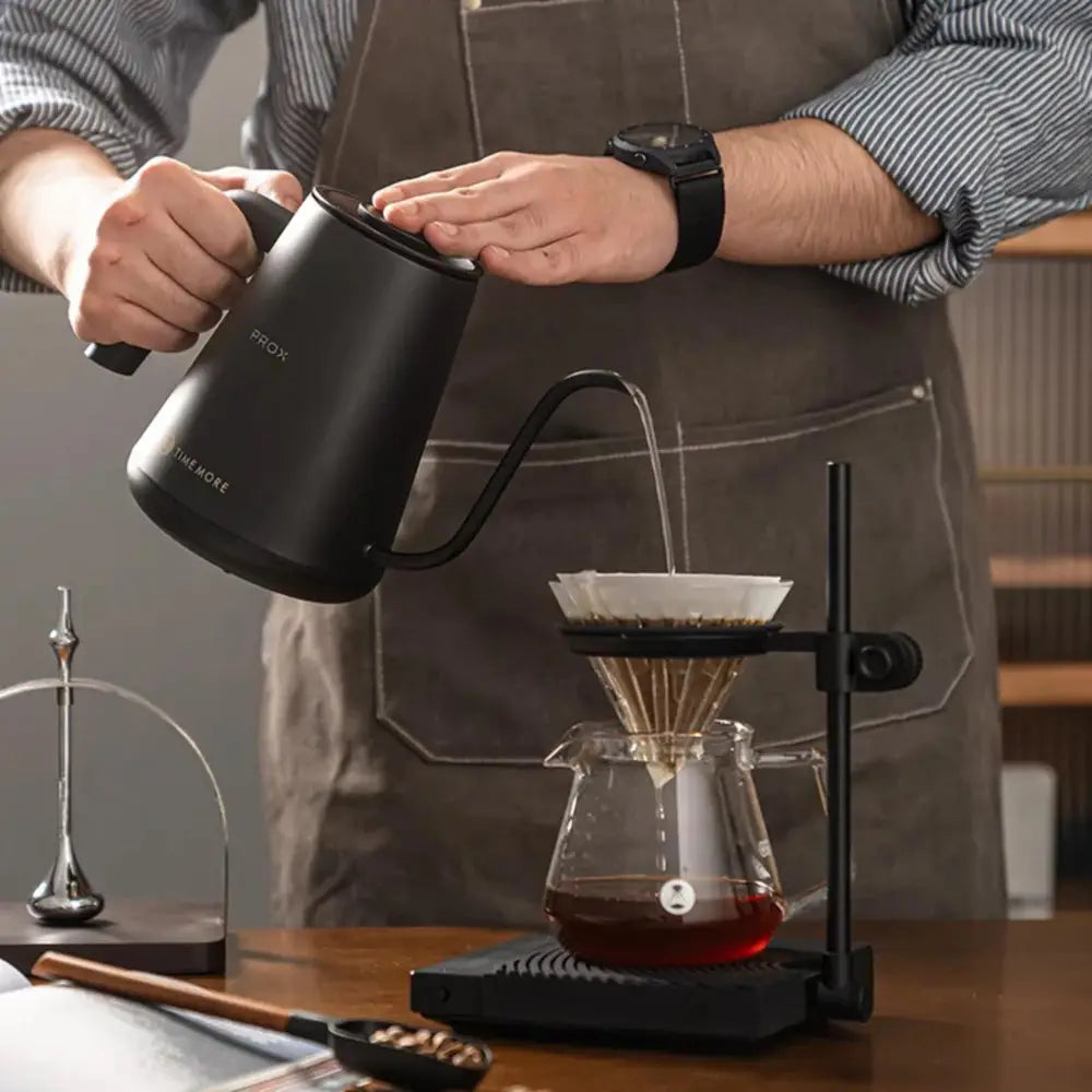 Person pouring coffee from a black pour-over coffee maker into a glass carafe.