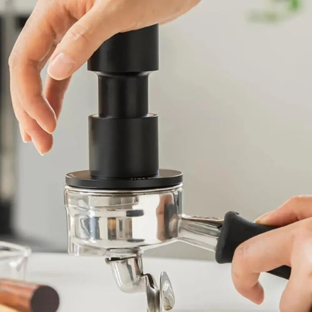 Person using a manual espresso grinder with a blurred kitchen background