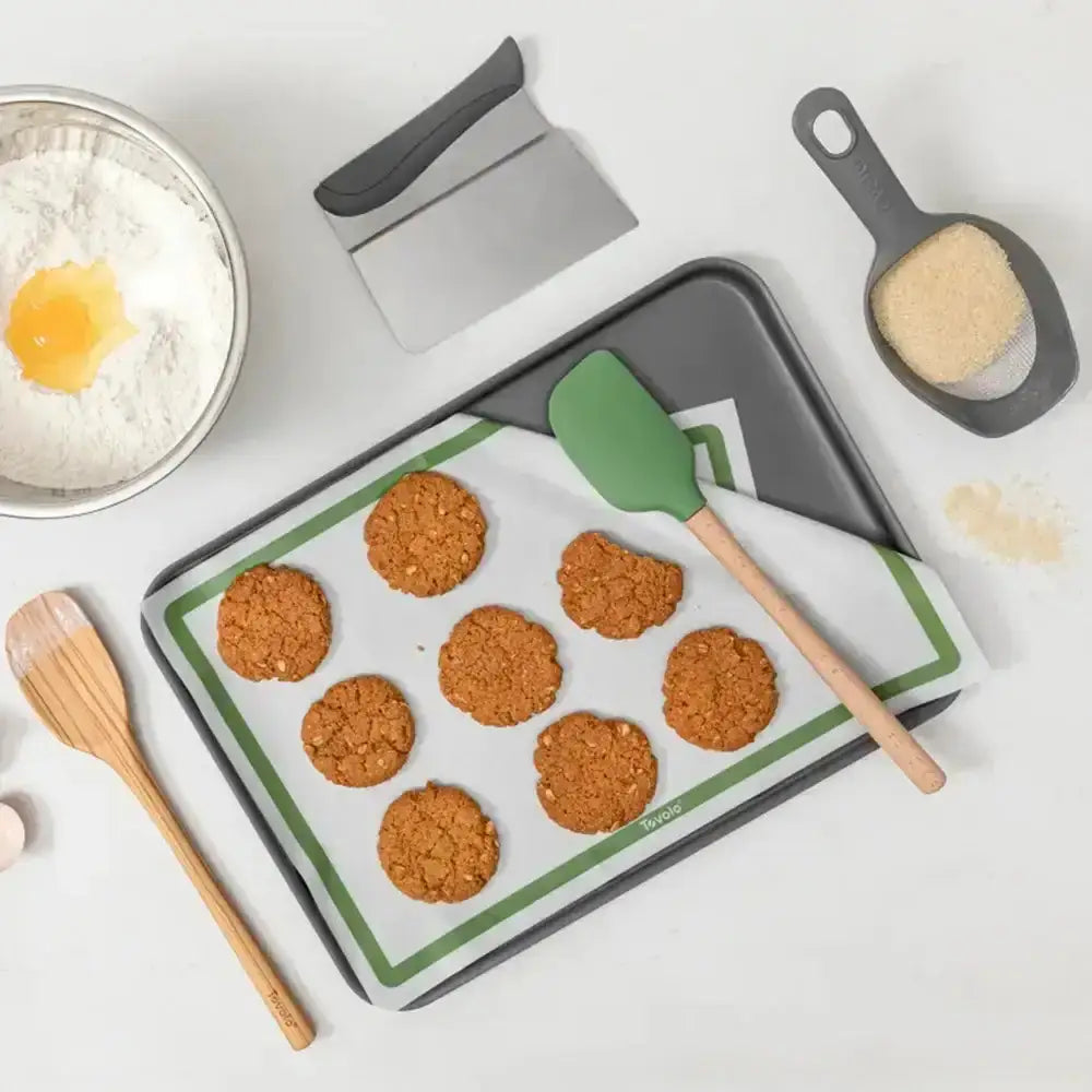 Baking tray with cookies, spatula, and measuring cup on a white surface