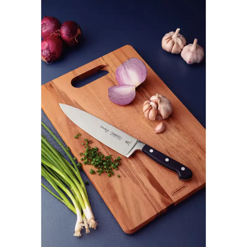 Wooden cutting board with a chef's knife, chopped onions, garlic, and green onions on a dark blue background.