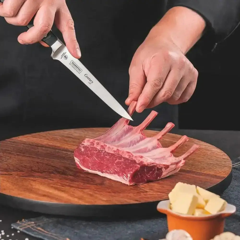 Person cutting raw lamb chops on a wooden board with a knife.