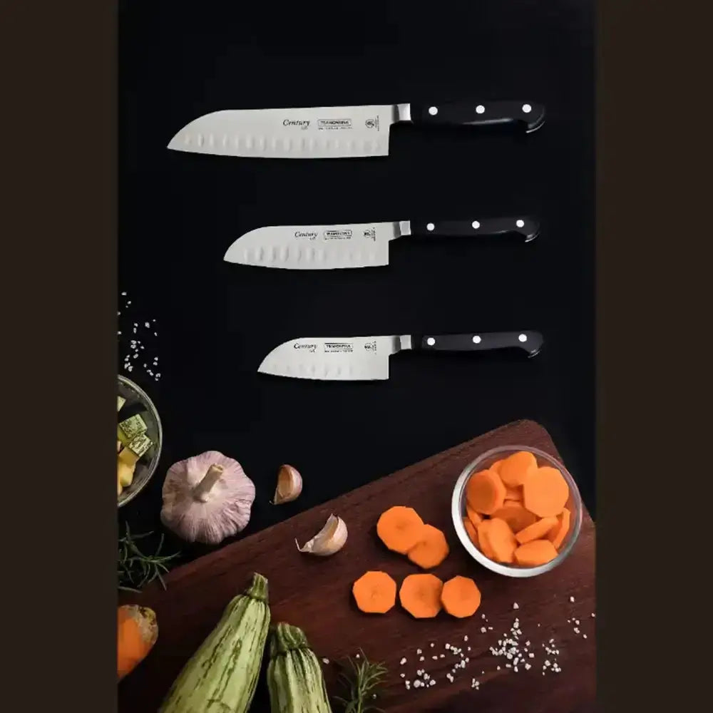 Set of knives on a dark surface with vegetables and a cutting board.