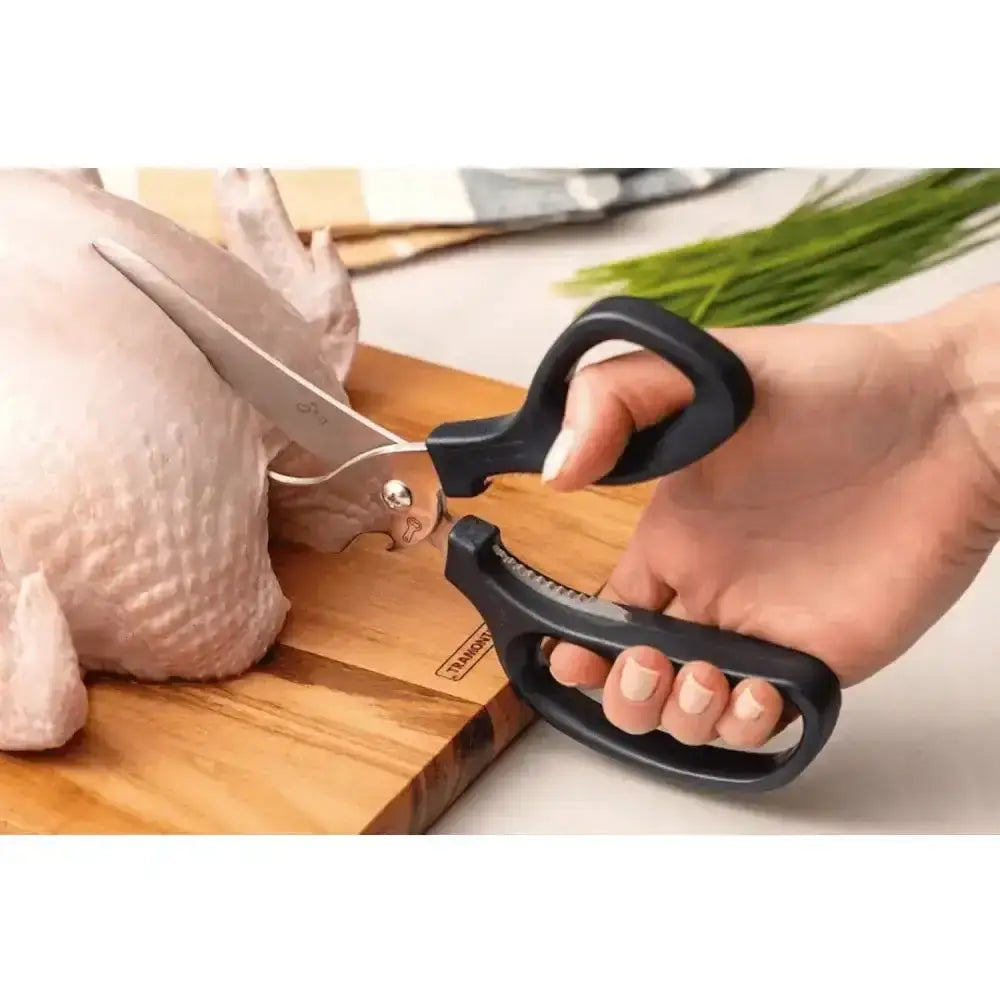 Person using kitchen shears to cut a chicken on a wooden cutting board.