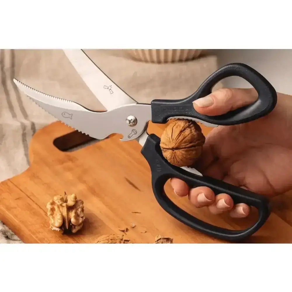 Hand holding a pair of black-handled scissors with a wooden cutting board and walnuts.
