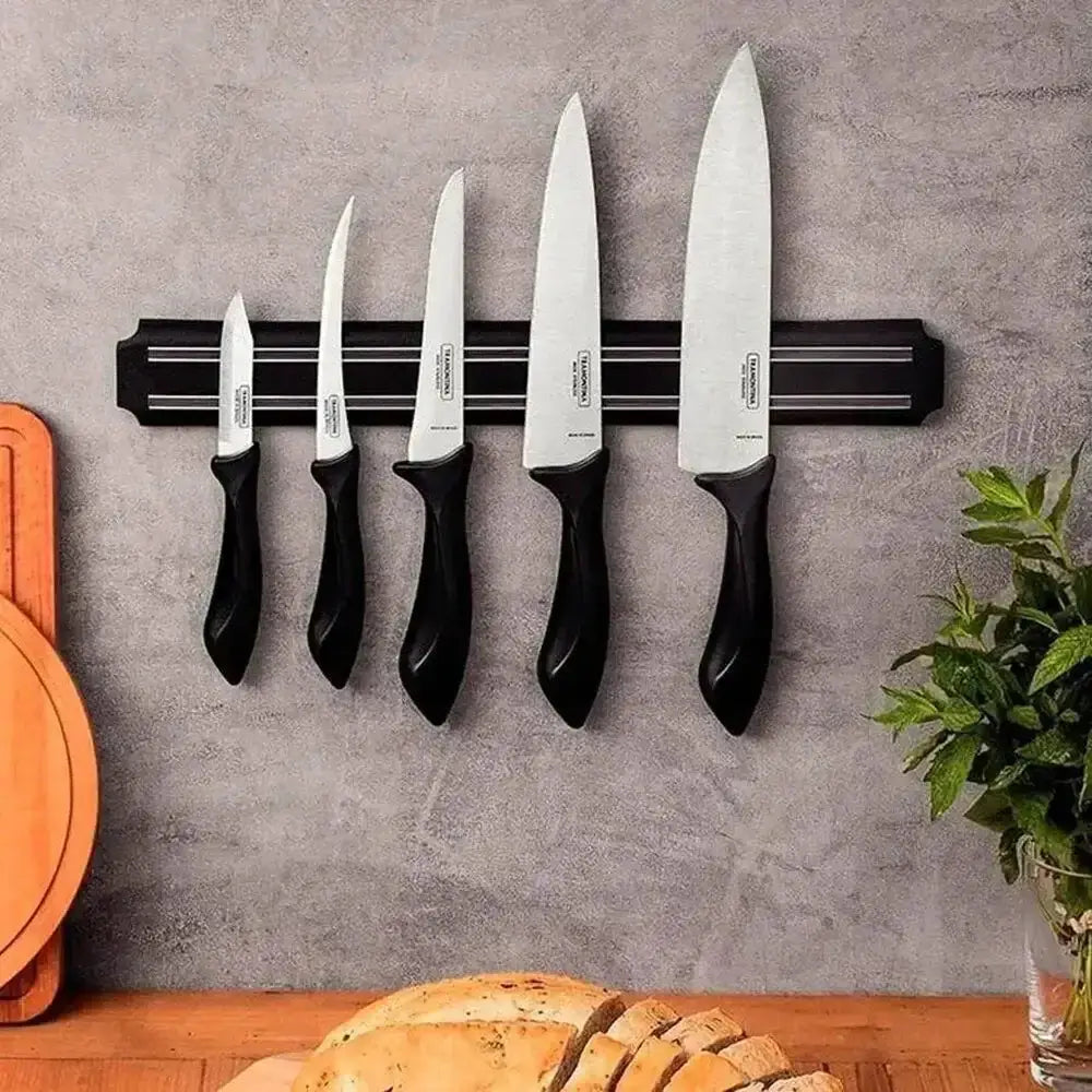 Set of knives on a magnetic strip against a gray wall with a wooden surface and plant in the foreground.
