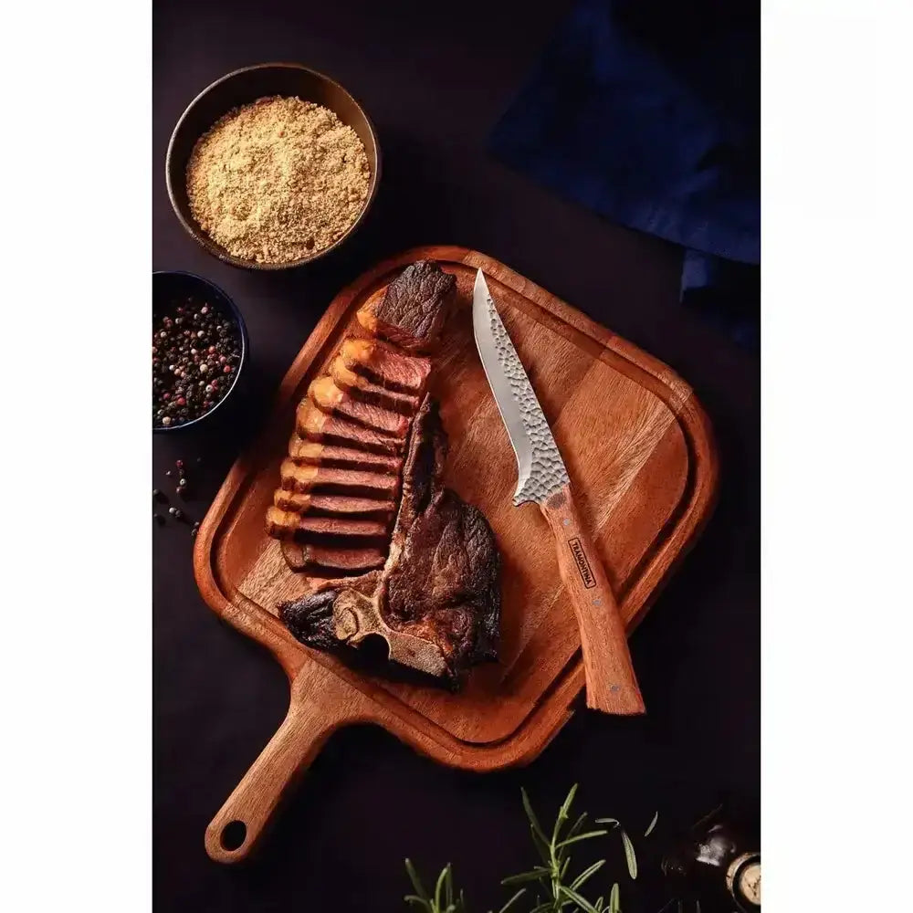 Grilled steak on a wooden cutting board with a knife, seasonings, and herbs on a dark surface.